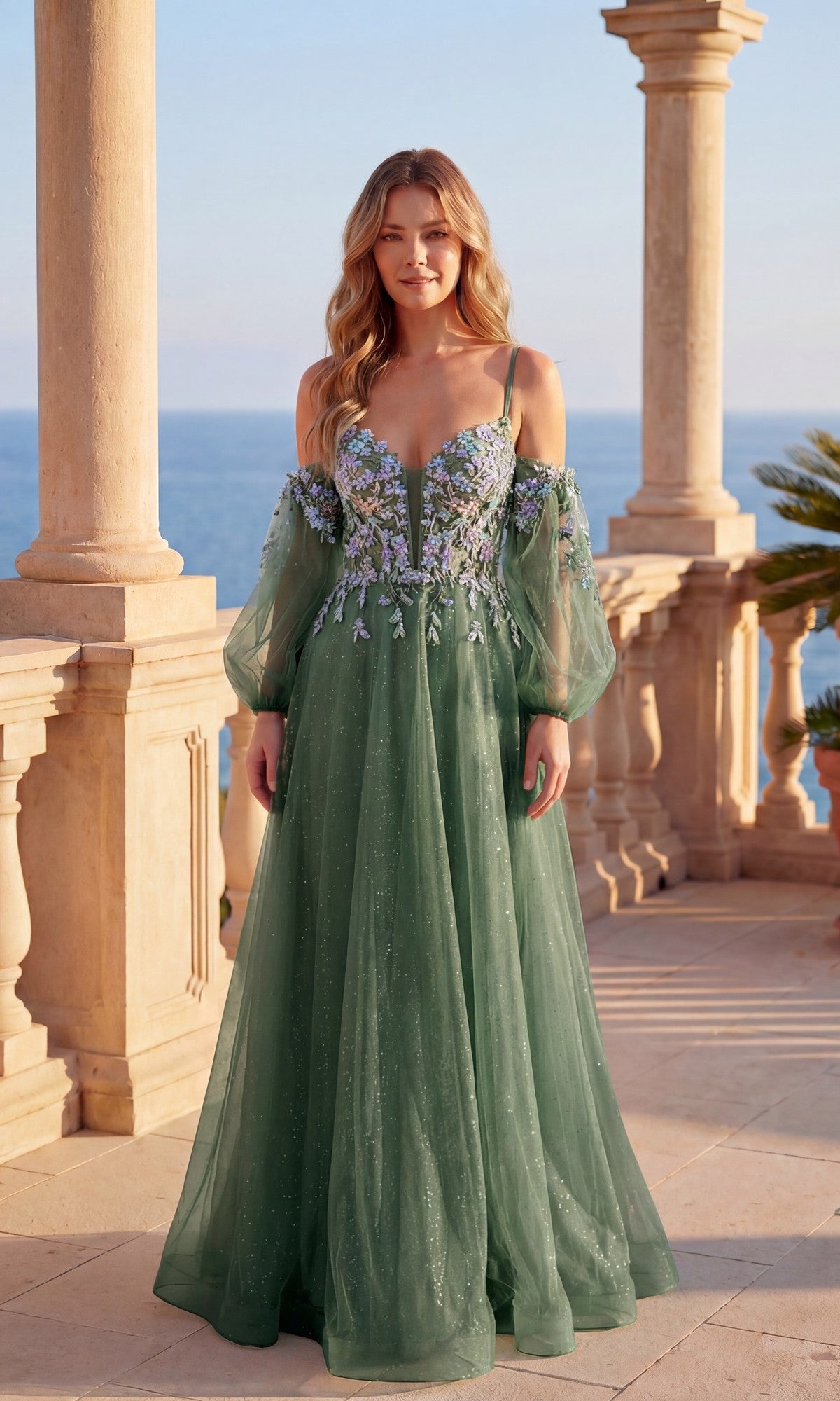 A woman in a dark sage Long Formal Dress: Chicas C358 with glitter tulle, floral embroidery, and sheer sleeves stands on a stone terrace overlooking the sea.